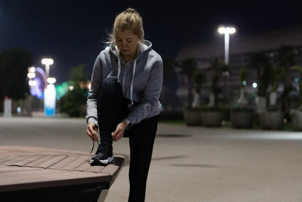 Female Runner in the city on a dark road pausing to tie shoe