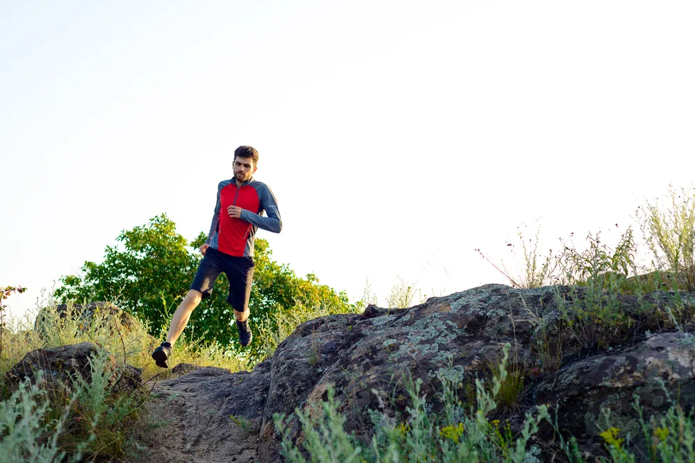 Man running rocky trail wearing hydration pack and fitness gear
